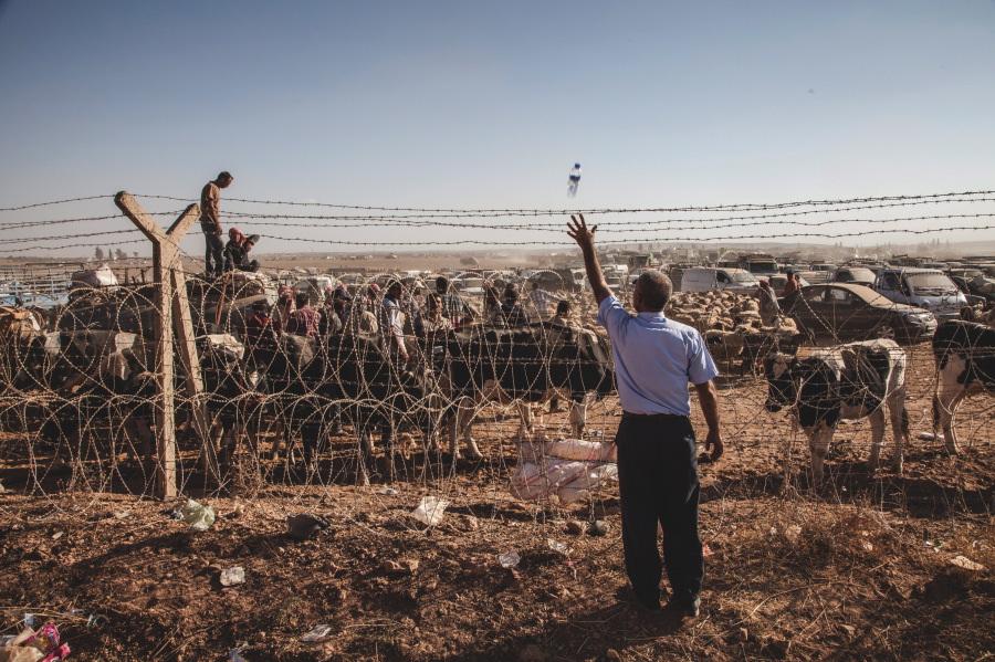 Un ciudadano lanza una botella de agua a un grupo de refugiados al otro lado de la frontera entre Turquía y Siria