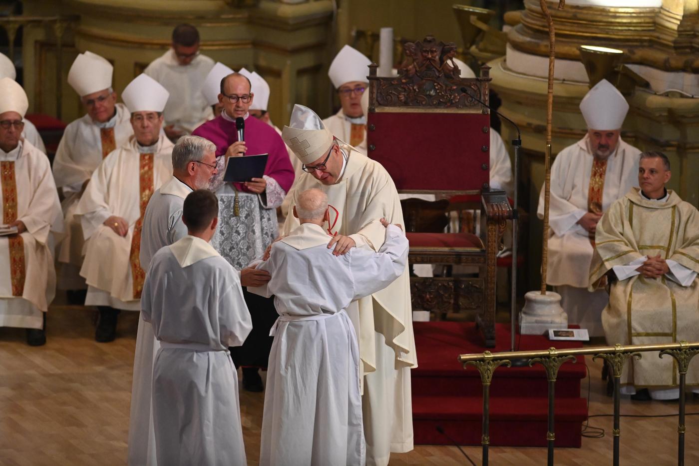 El sacerdote mayor y uno de los más jóvenes saludan al nuevo Obispo en su toma de posesión